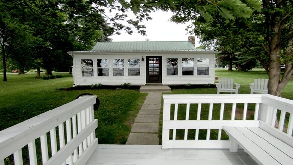 A white building with a green roof, surrounded by trees and a grassy lawn.