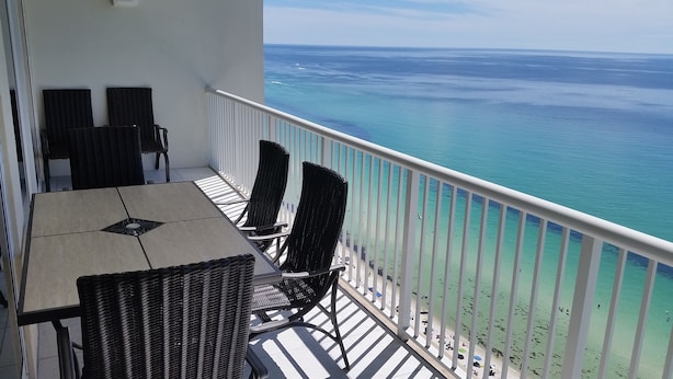 A balcony with a table and chairs, overlooking a clear blue sea. - TOP FLOOR, GREAT VIEW, FRIENDLY PRICES! (Panama City Beach)