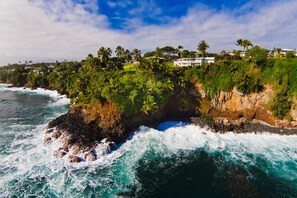 A coastal property with a rocky shoreline, lush greenery, and a view of the ocean.