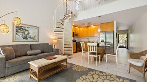 Amplia sala de estar con sofá, una mesa de centro y una mesa de comedor con sillas. Una escalera en espiral conduce a un nivel superior.