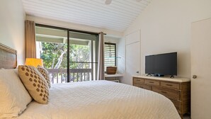 Un dormitorio con una cama grande, un televisor en una cómoda y un balcón con vistas a árboles.