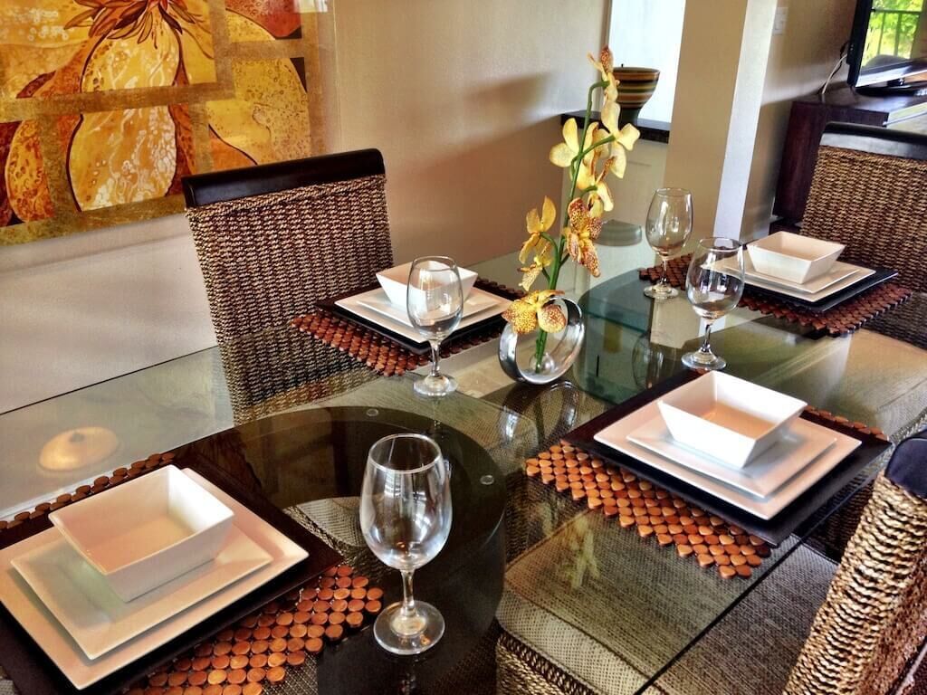 A dining table set with white plates, bowls, and wine glasses, surrounded by wicker chairs.