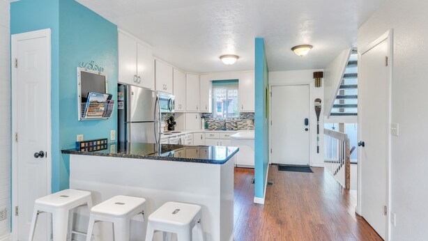 A modern kitchen with white cabinets, a blue accent wall, and a central island with bar stools. - Large Townhouse, 3Bd/3Ba, Near BYU Stadium/BYU  (Provo)