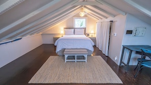 Une chambre à coucher comprenant un lit, des tables de chevet, un bureau, une fenêtre et un ventilateur de plafond.