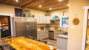 Una cocina con una amplia mesa de madera, armarios blancos y un refrigerador de acero inoxidable.