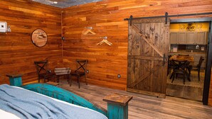 Una habitación rústica con paredes de madera, una cama, un comedor y una cocina visible a través de una puerta corredera.
