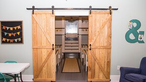Una habitación con una puerta corredera de madera que da a una escalera. Hay un cuadro con banderas coloridas en la pared, un sofá azul y una mesa blanca con sillas verdes.