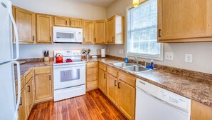 Une cuisine avec des meubles de rangement en bois, un réfrigérateur blanc, un four à micro-ondes, une cuisinière, un évier et un lave-vaisselle.