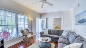Un salon avec un canapé d’angle gris, un fauteuil en osier, une table basse ronde et un ventilateur de plafond.