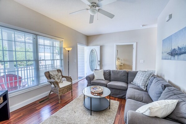 A living room with a gray sectional sofa, a wicker chair, a round coffee table, and a ceiling fan.