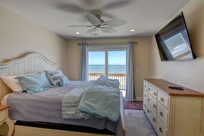Quarto com cama, cômoda, TV fixada na parede e vista para o oceano pela janela.