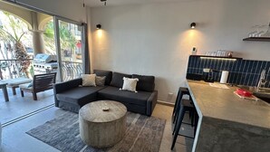 A modern living room with a sectional sofa, a round coffee table, and a kitchen area with a bar counter. - BRAND NEW Remodel & BEST Oceanfront BEACH/SURF Location In Cabo!!! (San José del Cabo)