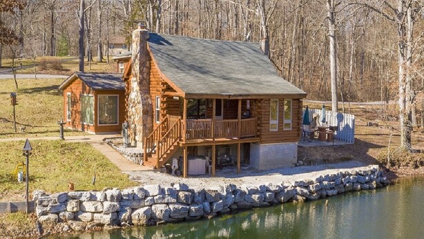 A log cabin with a balcony and a stone wall in front. - Authentic Log cabin with something for everyone! (Marthasville)