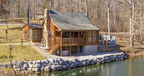 A log cabin with a balcony and a stone wall in front.