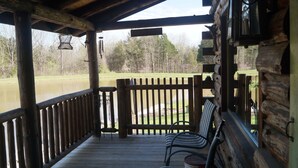 A wooden deck with a railing, a bench, and a hanging lantern. - Authentic Log cabin with something for everyone! (Marthasville)