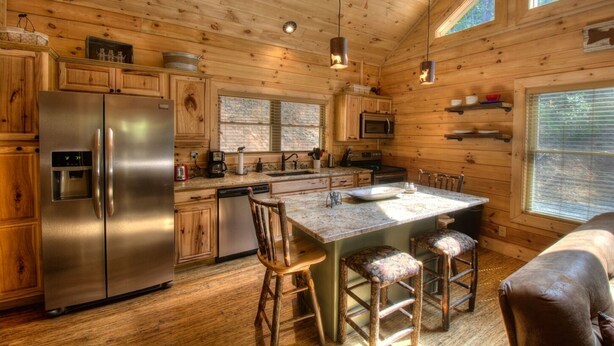 A cabin-style kitchen with wooden walls, a stainless steel refrigerator, a microwave, and a central island with bar stools.
