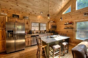 A cabin-style kitchen with wooden walls, a stainless steel refrigerator, a microwave, and a central island with bar stools. - Luxury Honeymoon Suite-10 min from Smoky Mtn Railway & NOC (Bryson City)
