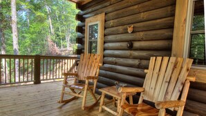 A log cabin with a wooden porch featuring two rocking chairs and a small table.