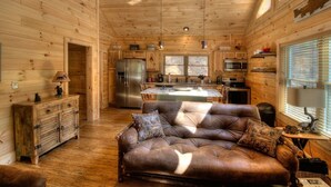 A cozy cabin interior with a central island, wooden walls, a leather sofa, and a refrigerator.