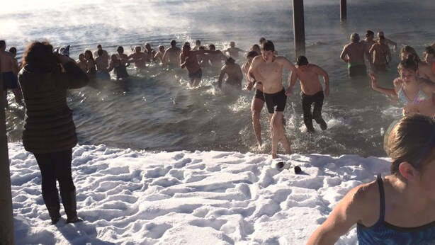 Een groep mensen in een besneeuwde omgeving, mogelijk een meer of rivier, met bergen op de achtergrond.
