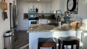 A modern kitchen with white cabinets, stainless steel appliances, granite countertops, and a decorative rooster. - PGA West La Quinta STR #068246 - Close to Golf, Tennis & Music Festivals (La Quinta)