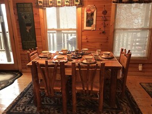 A wooden cabin interior with a dining table set for six, surrounded by wooden chairs.