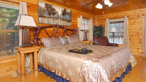 A wooden cabin bedroom with a large bed, two nightstands, a ceiling fan, and a painting on the wall.