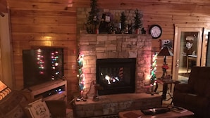 A cozy cabin interior with a stone fireplace, a television, and festive decorations.