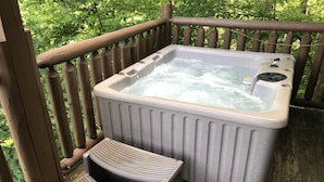 A hot tub on a wooden deck with a wooden railing and a small wooden bench.