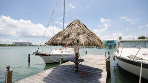 Un muelle de madera con un paraguas de paja, barcos amarrados y cielo despejado.
