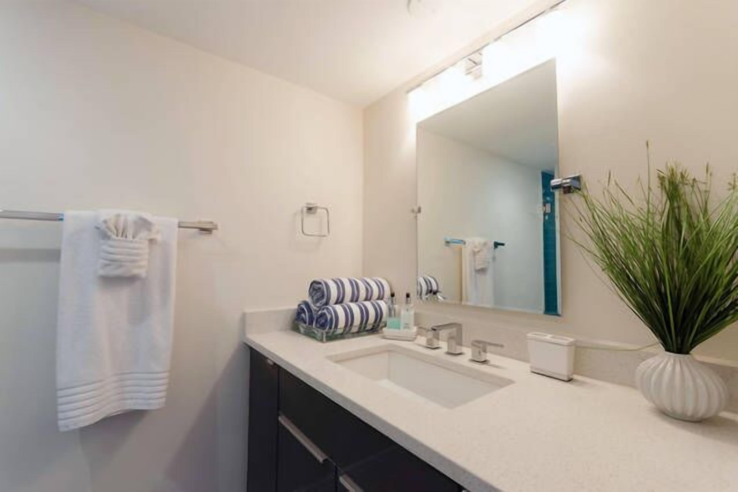 A modern bathroom with a white sink, a large mirror, and a towel rack.