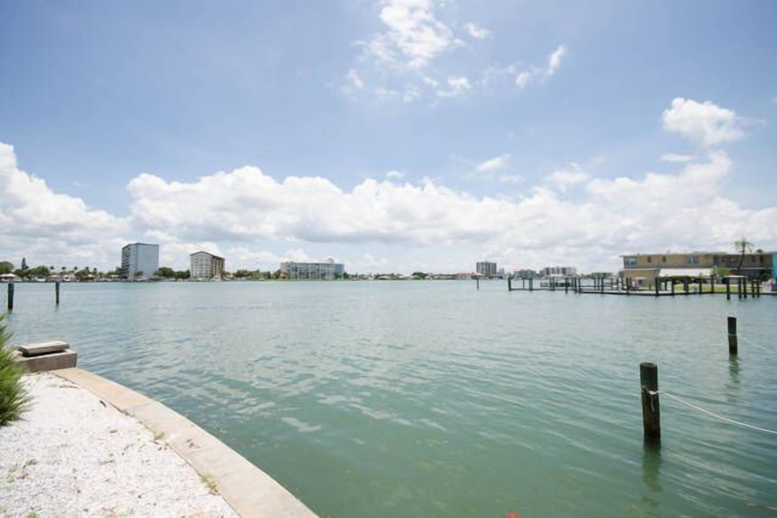 A waterfront view with a calm body of water, a sandy shore, and buildings in the background.