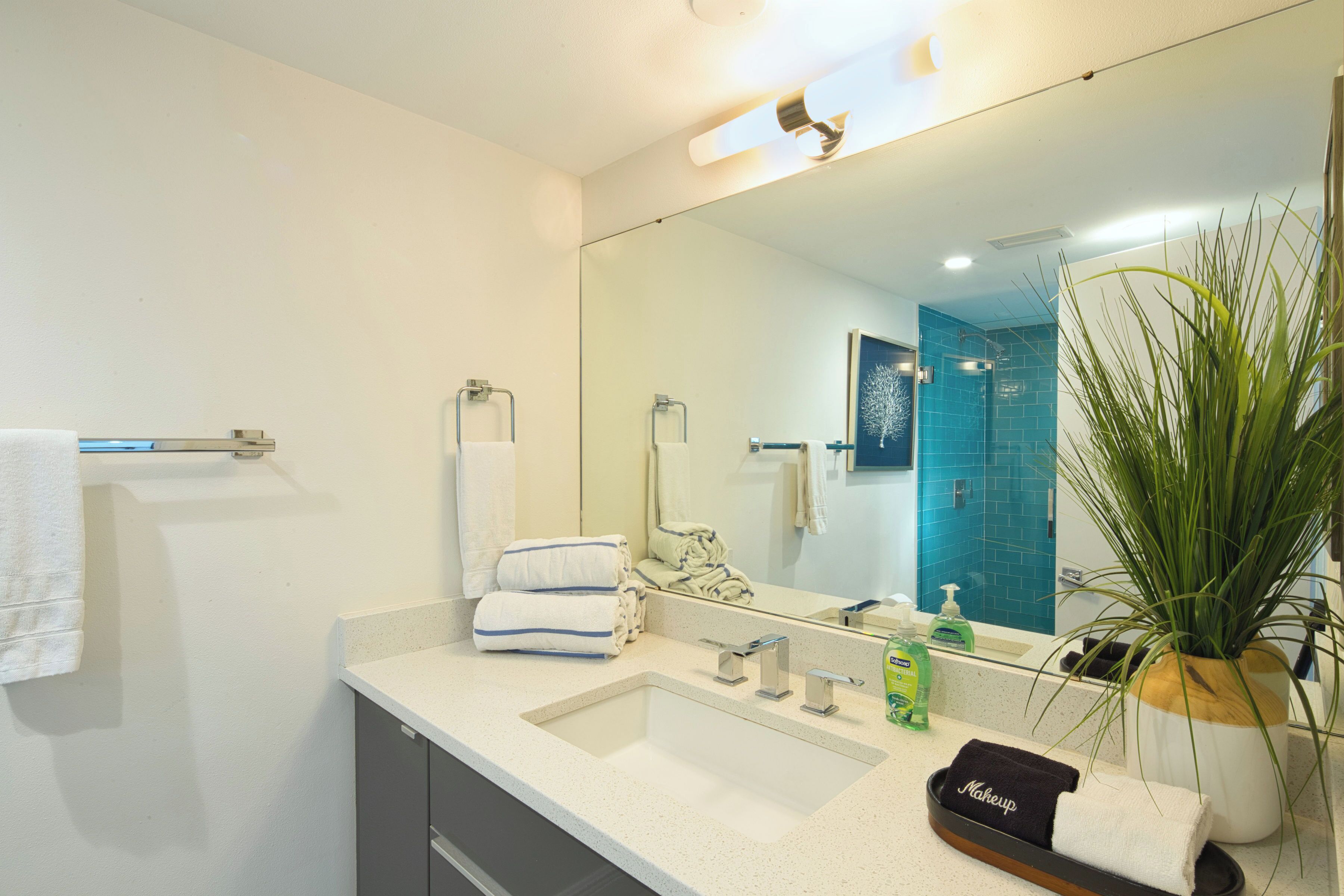 Un bagno moderno con uno specchio grande, due lavandini, un porta asciugamani, una pianta in vaso e una trousse da trucco sul ripiano.