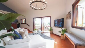 Ein geräumiges Wohnzimmer mit einem weißen Sofa, einer Bank, einem Esstisch und einem großen Fenster.