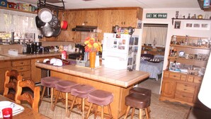 A kitchen with wooden cabinets, a refrigerator, a bar area with stools, and a dining table with chairs.