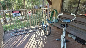 A wooden deck with a stationary bike and a bicycle leaning against a fence. There are signs warning against climbing and feeding bears.