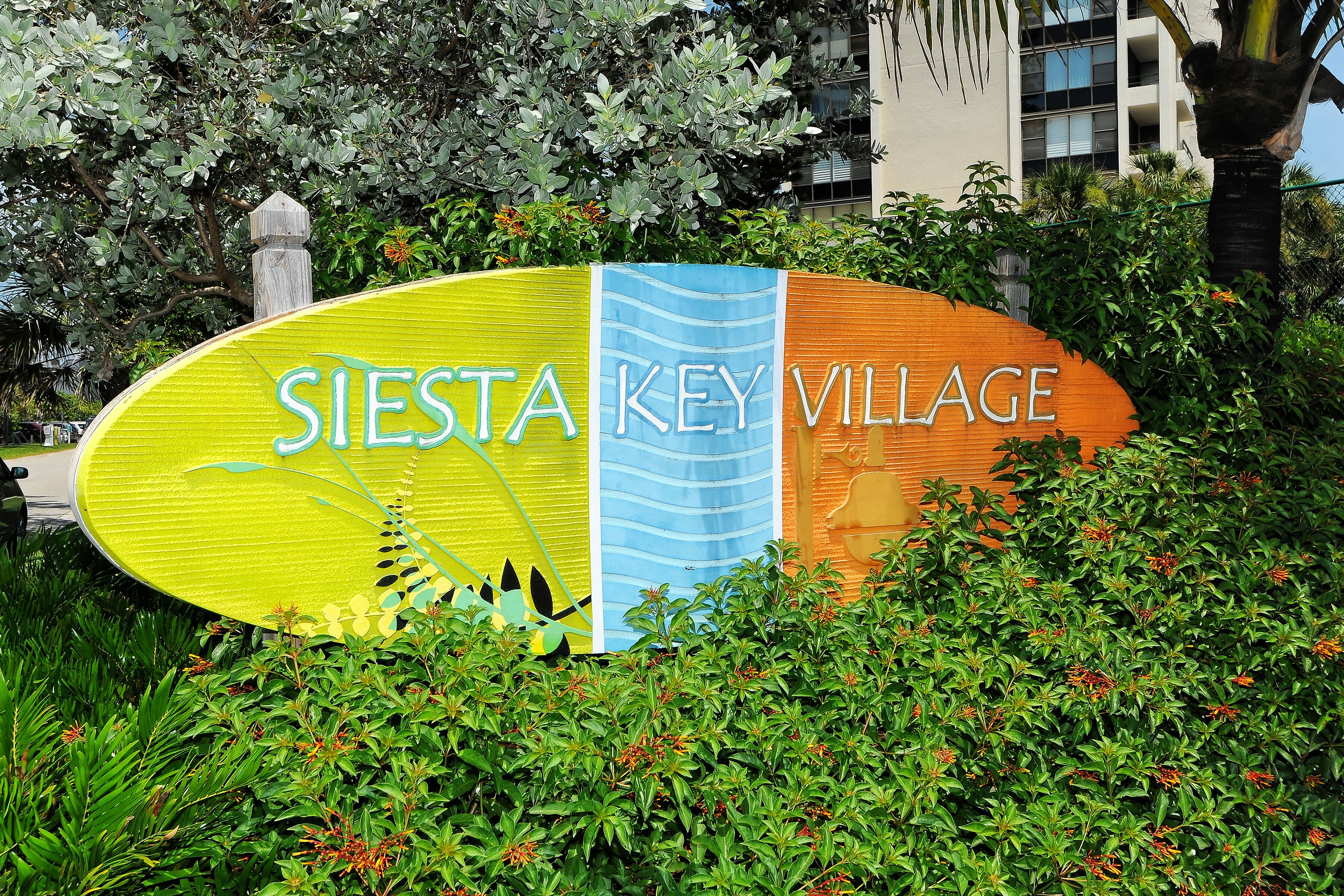 A sign for Siesta Key Village with a colorful design and greenery around it.