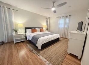 A bedroom with a bed, bedside tables, a TV, and a ceiling fan.