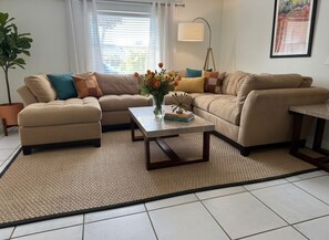 A living room with a beige sofa set, a coffee table, a floor lamp, and a potted plant.
