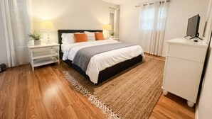 Un dormitorio con cama, mesitas de noche, televisor y ventilador de techo.