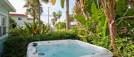 Un jacuzzi rodeado de abundante vegetación y un edificio residencial al fondo.