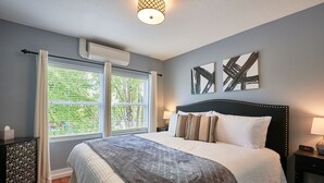 Ein Schlafzimmer mit einem Bett, zwei Nachttischen, einem Fenster mit Jalousien und einer Deckenleuchte.