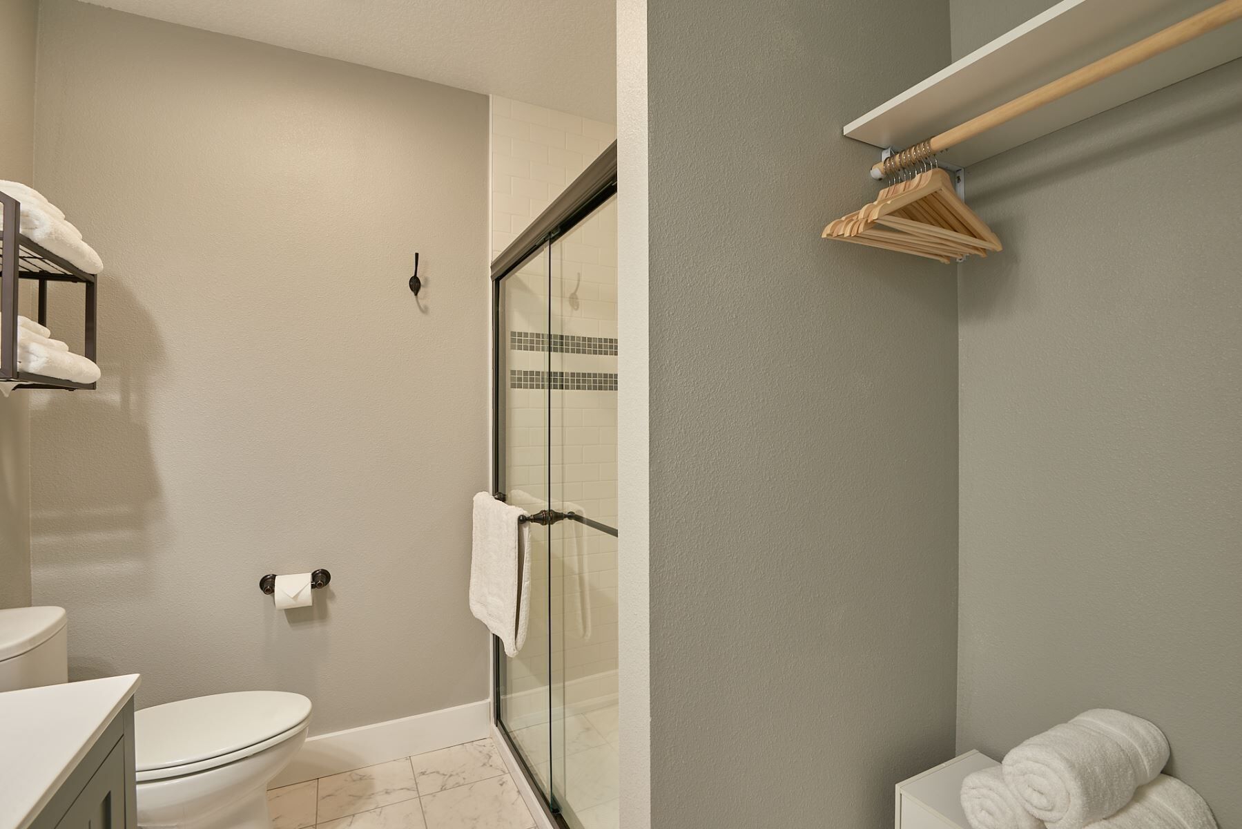 Un baño con inodoro, cabina de ducha de vidrio, toallero y esquinero para toallas.