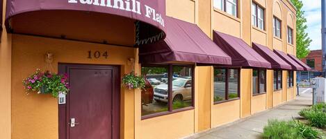 A row of Yamhill Flats with a number 104 entrance, awnings, and hanging flower baskets.