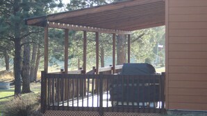 Eine überdachte Terrasse im Freien mit Grill, umgeben von Bäumen und einem Gebäude.