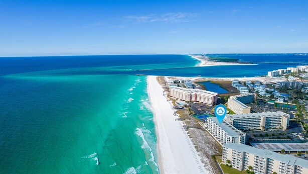 An aerial view of a coastal hotel with beachfront access, multiple buildings, and a clear view of the ocean.