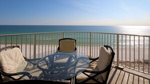 A balcony with a glass table and chairs overlooking a beach.