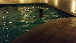 Une piscine où une personne nage, entourée d’un espace de détente extérieur et d’un bâtiment doté de grandes fenêtres.