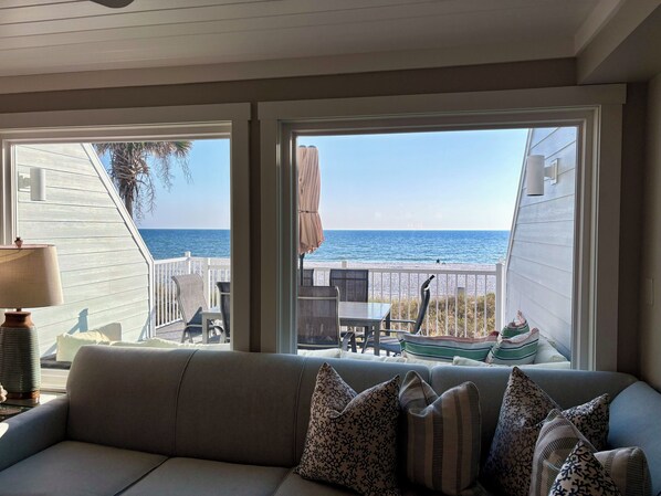 Enjoy ocean views from the large window in this room, featuring a sofa, table, chairs, and a lamp.