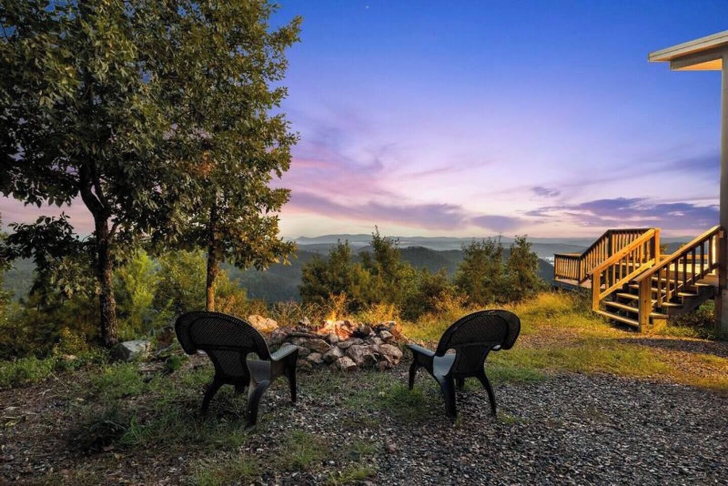 Een uitzicht op een berglandschap met een vuurkuil en twee stoelen die ervoor gericht staan.